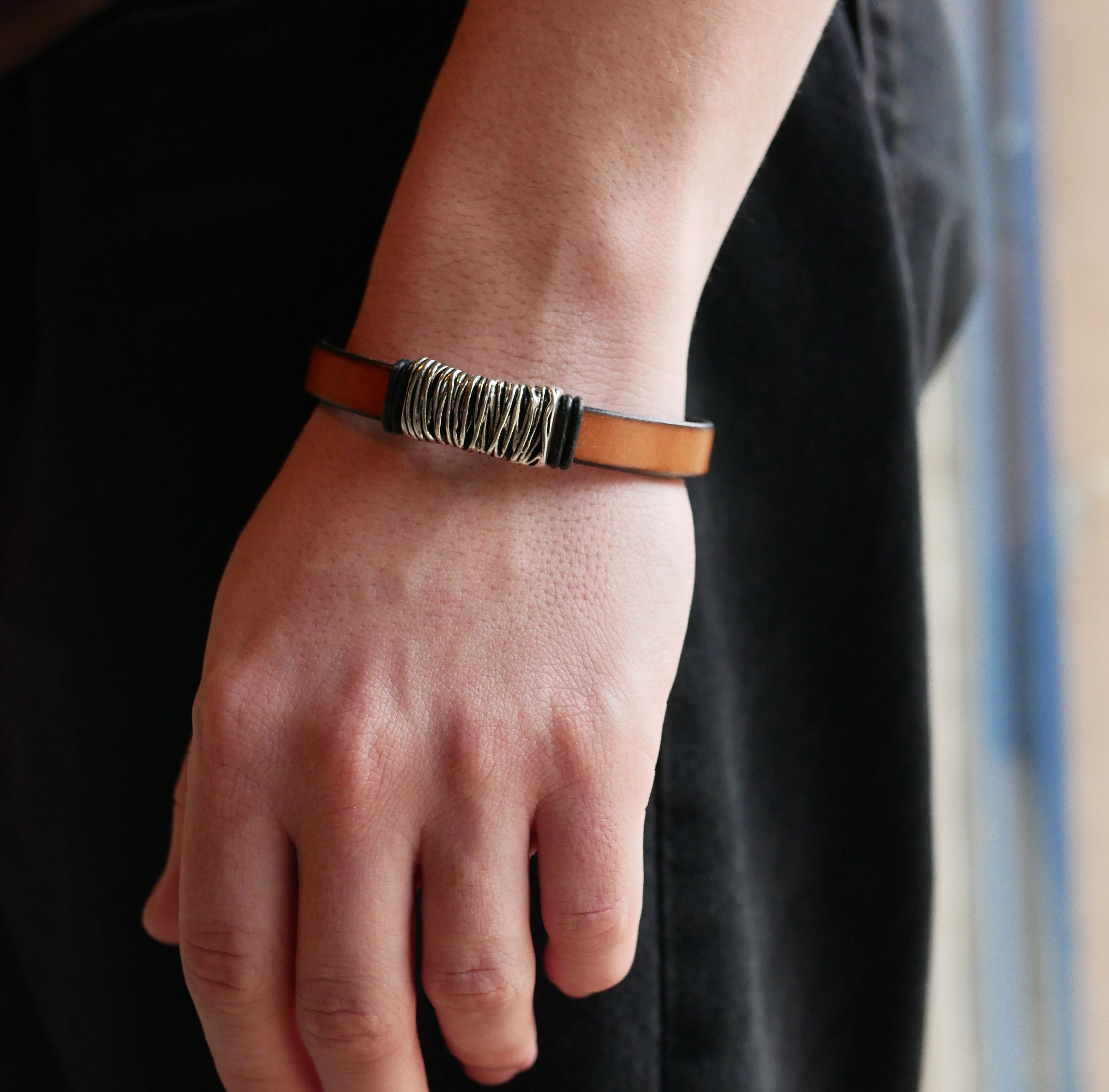 Band van camelkleurig leer met gevlochten metalen versiering en T-vormige sluiting