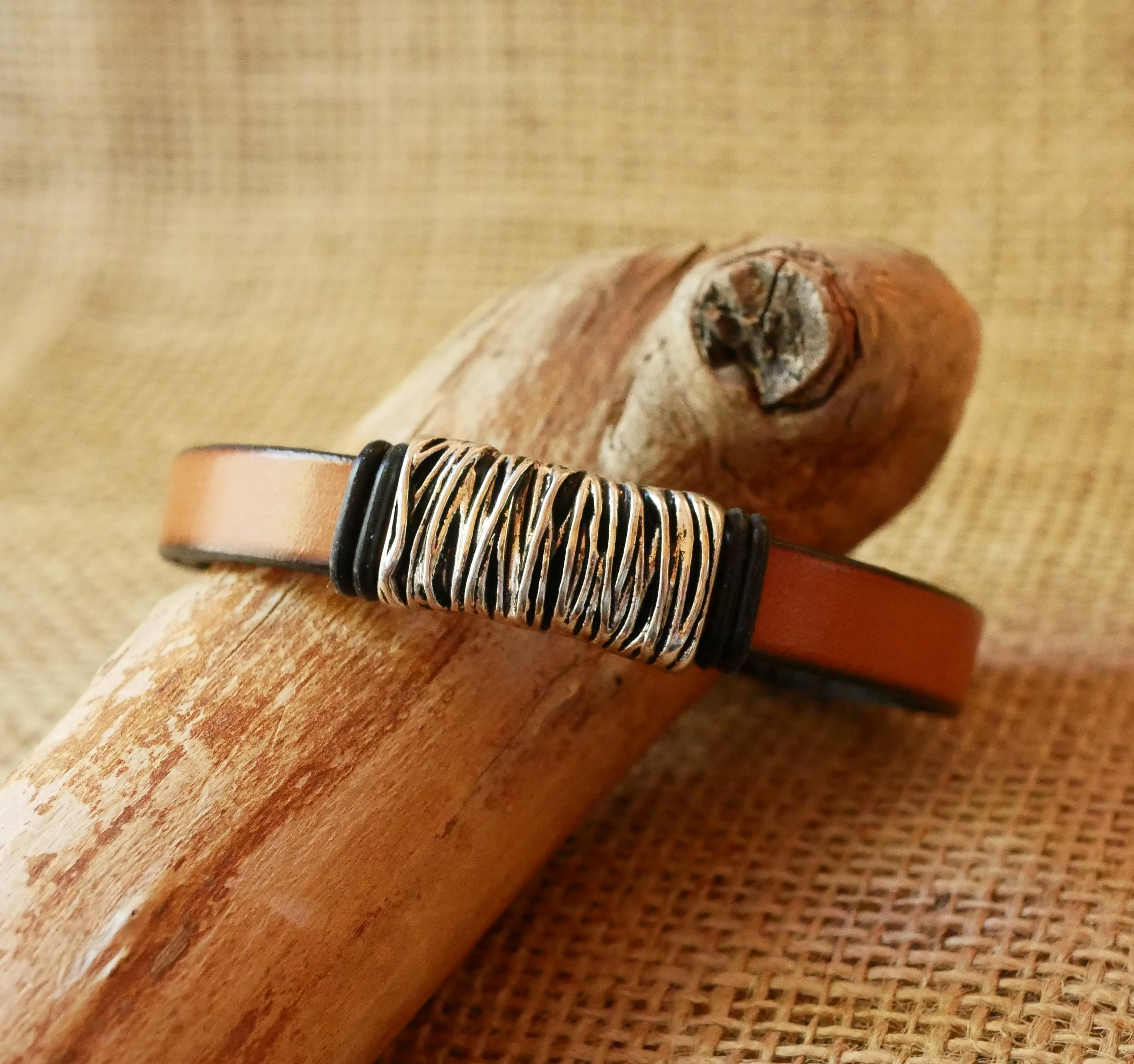 Band van camelkleurig leer met gevlochten metalen versiering en T-vormige sluiting