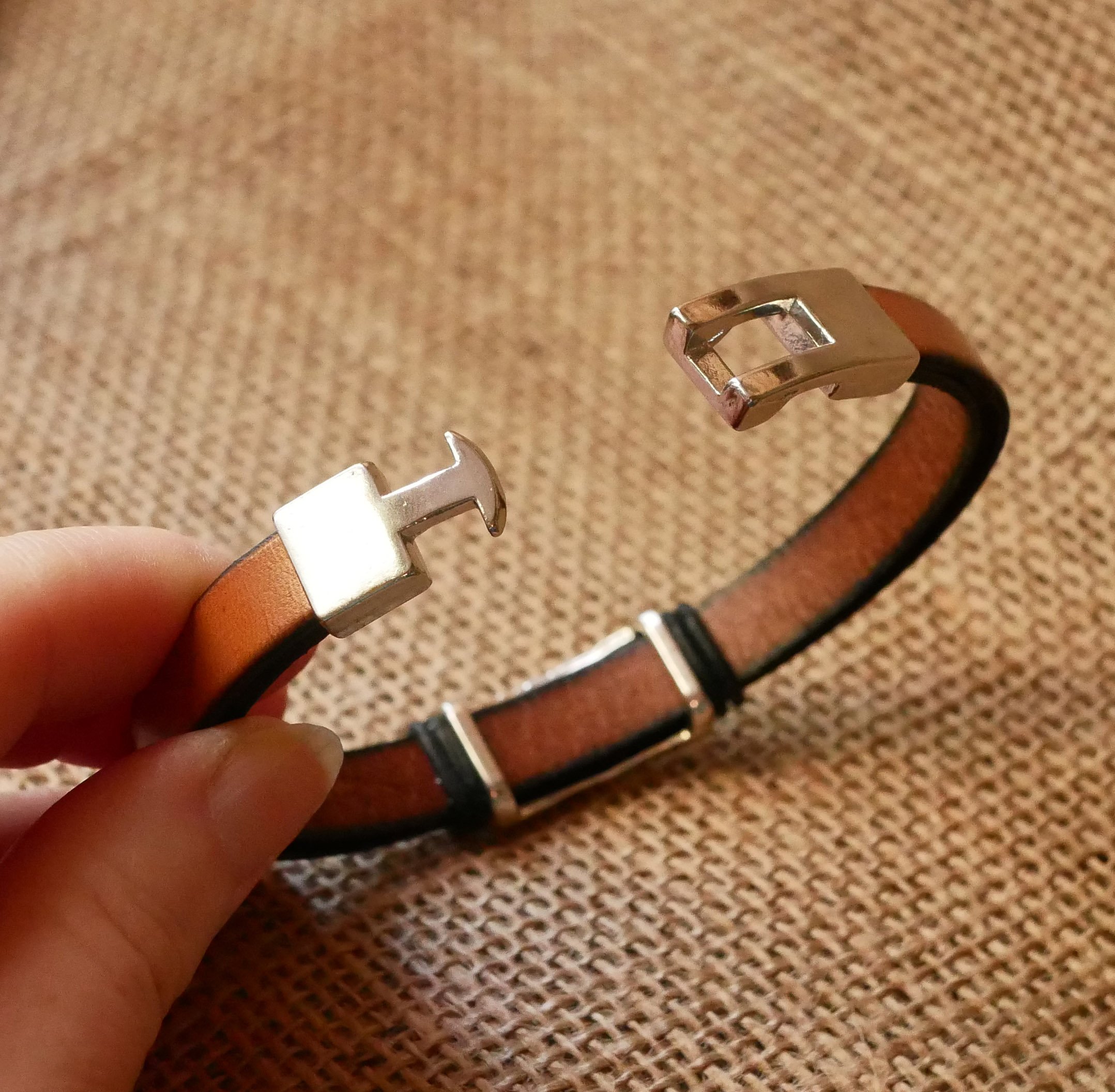 Band van camelkleurig leer met gevlochten metalen versiering en T-vormige sluiting