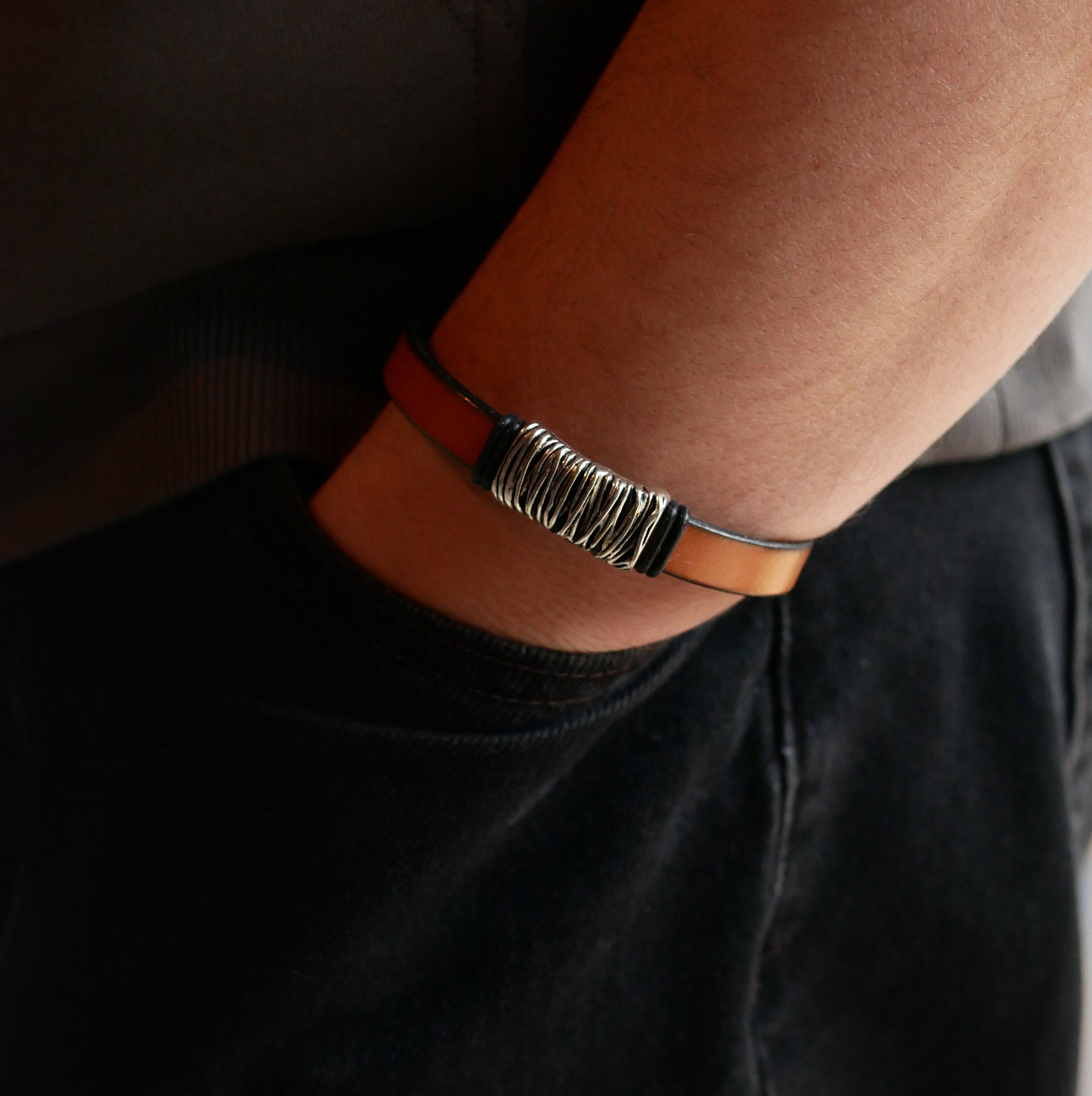 Band van camelkleurig leer met gevlochten metalen versiering en T-vormige sluiting