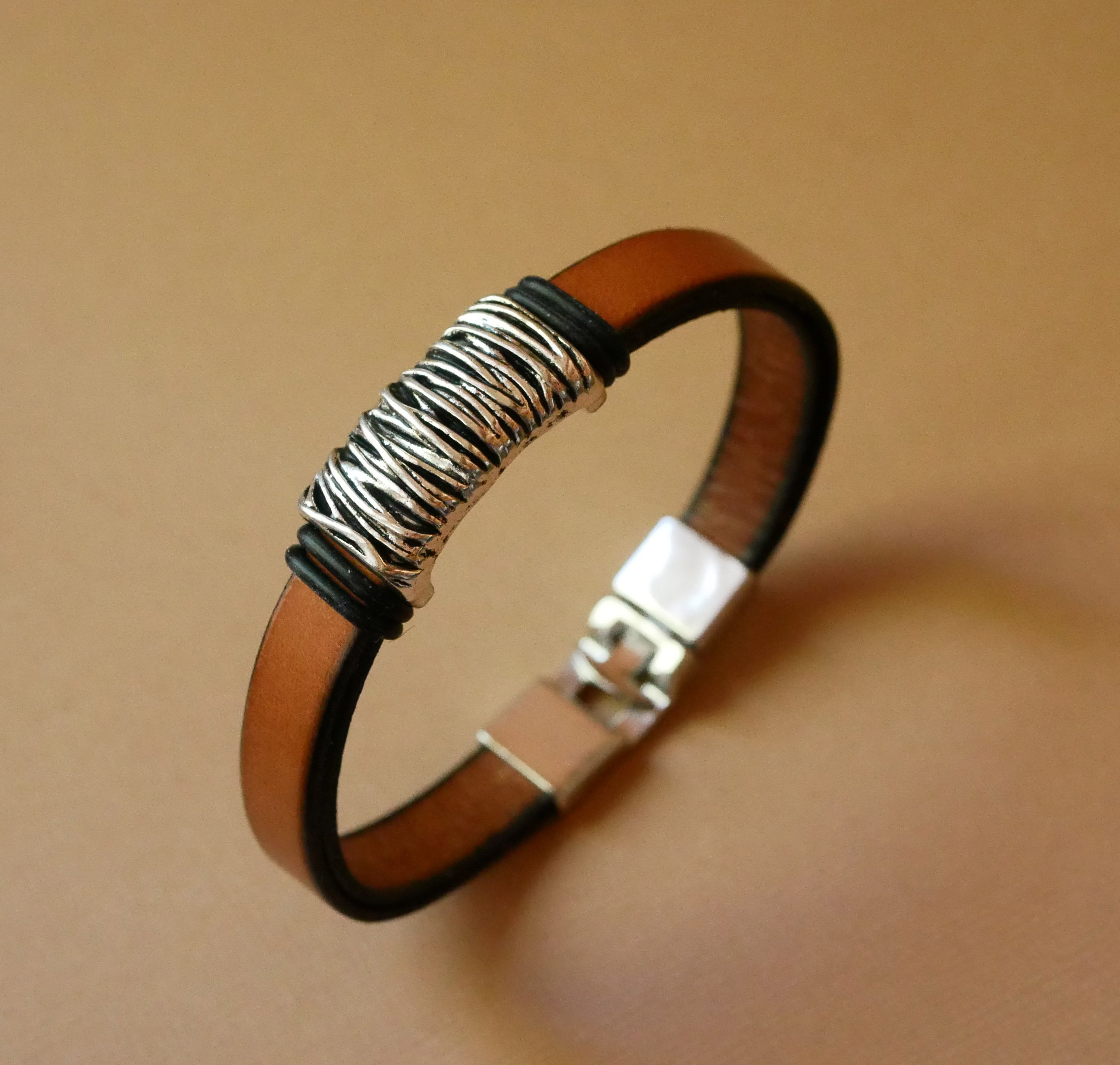 Band van camelkleurig leer met gevlochten metalen versiering en T-vormige sluiting