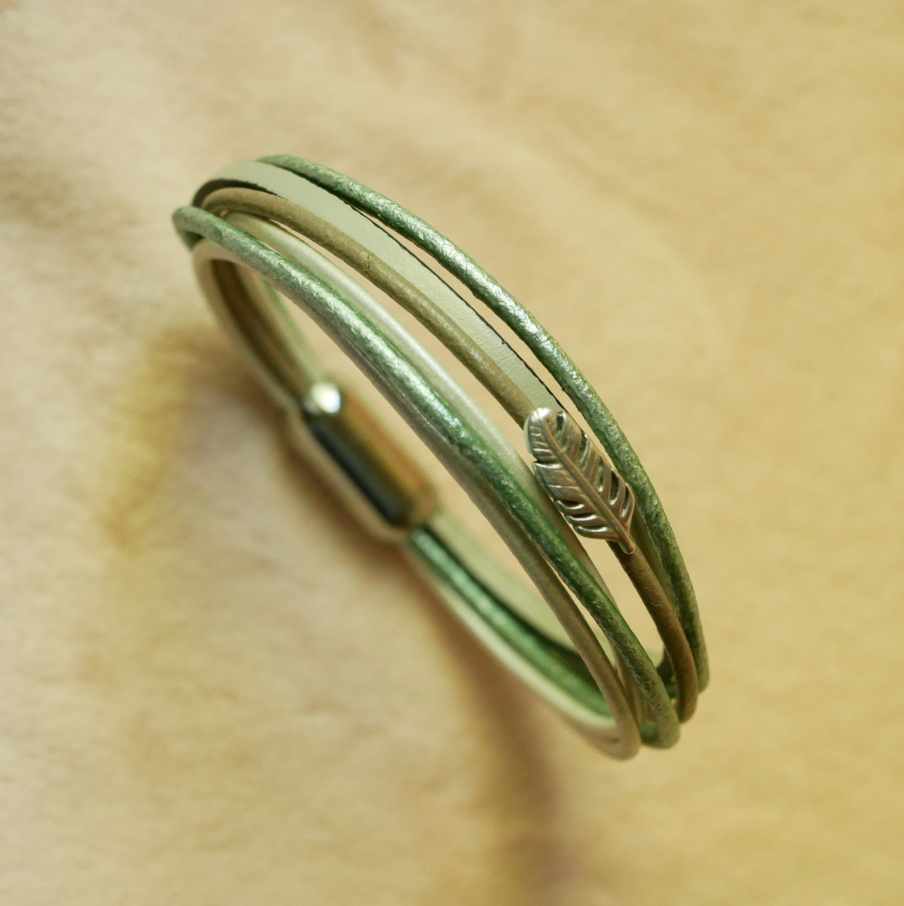 Multileren armband in beige, lichtgroen en parelmoer, versierd met een veertje