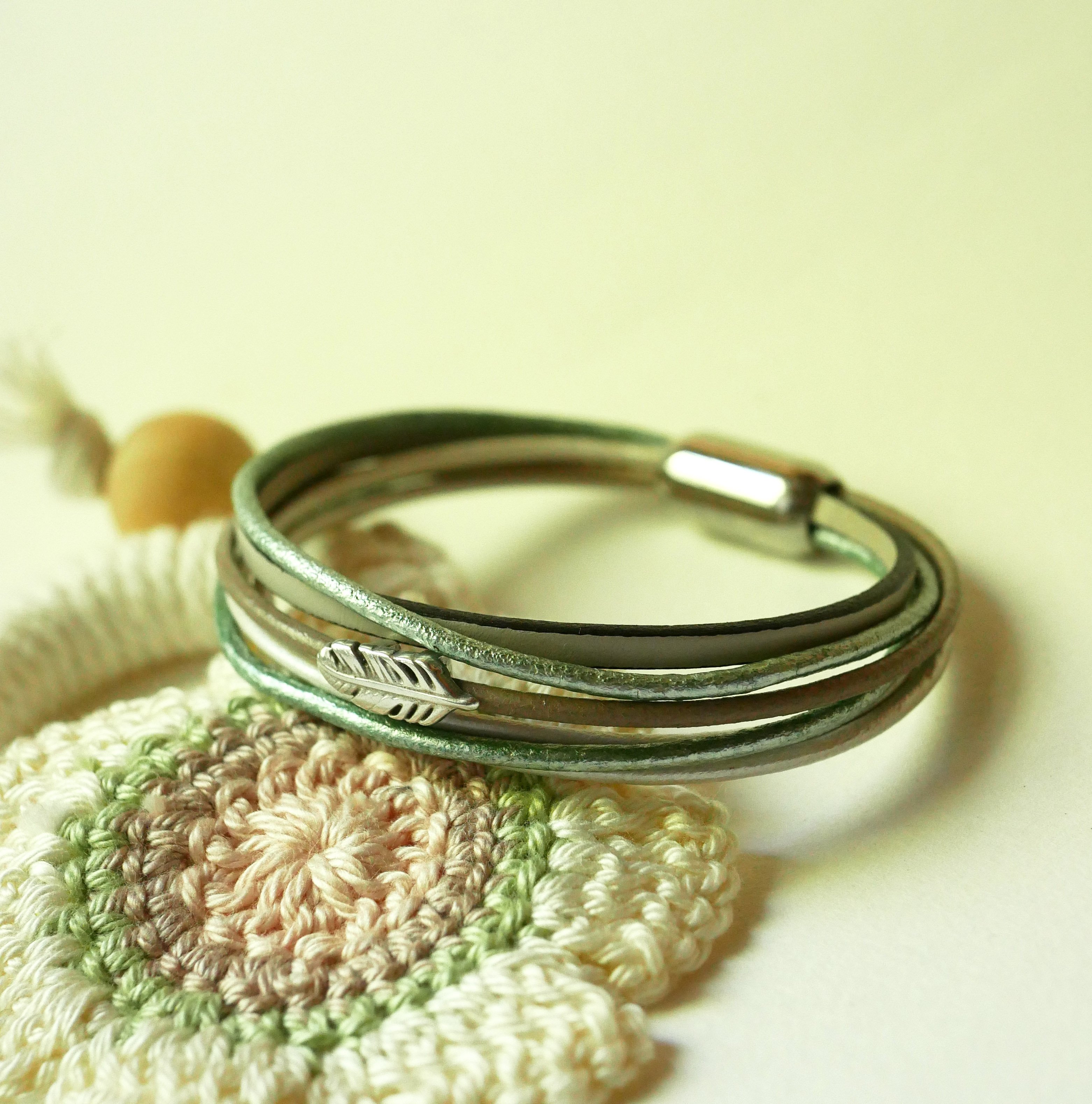 Multileren armband in beige, lichtgroen en parelmoer, versierd met een veertje
