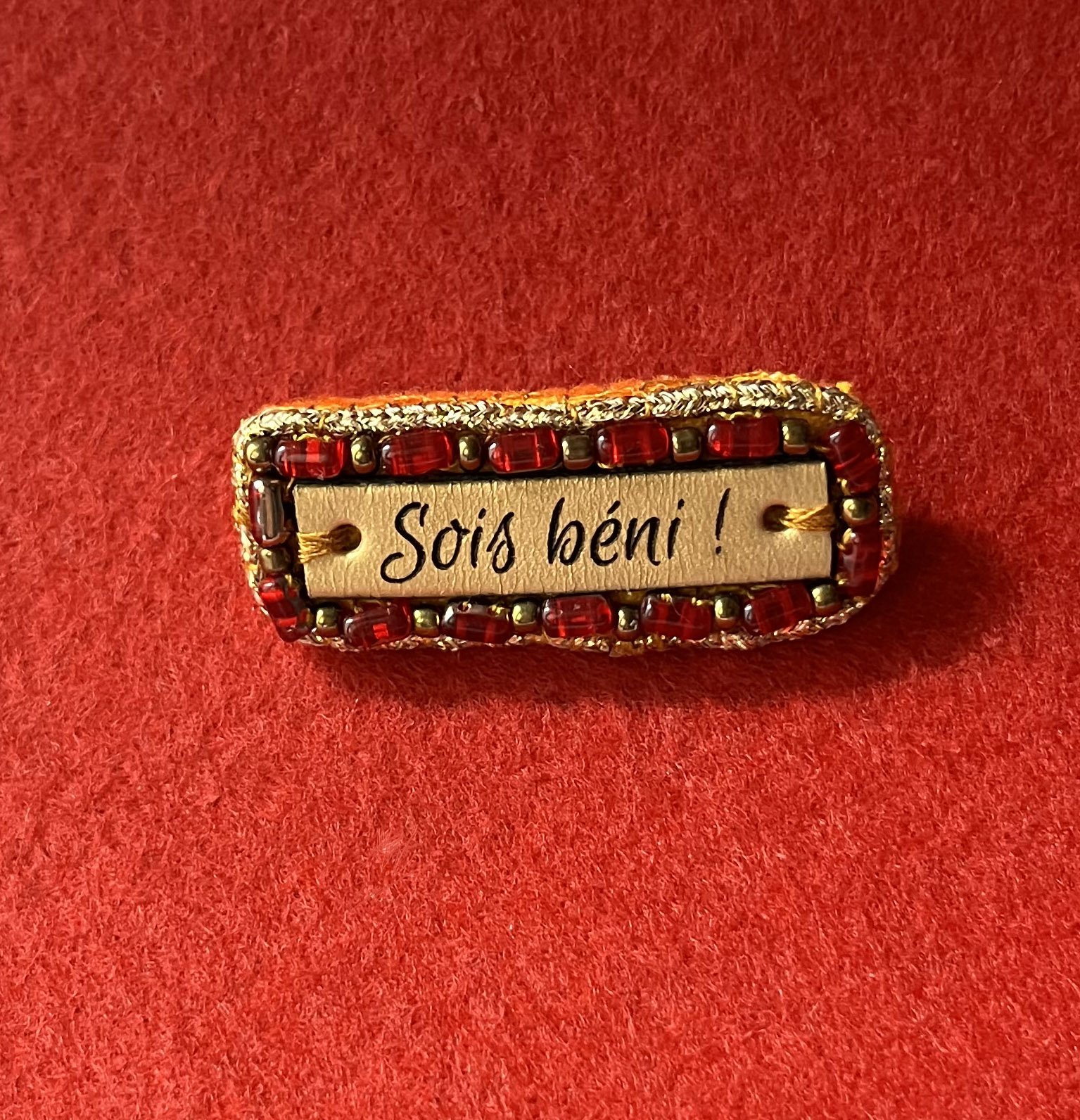 Broche &agrave; message en cuir grav&eacute; "sois b&eacute;ni" en perles rouges et dor&eacute;es 